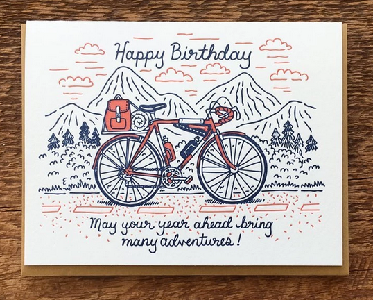 Birthday card with cream background and drawing of salmon colored bicycle in front of mountains
