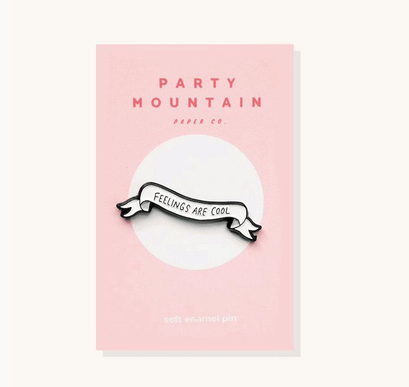 a black and white soft enamel pin that looks like a ribbon banner that says feelings are cool